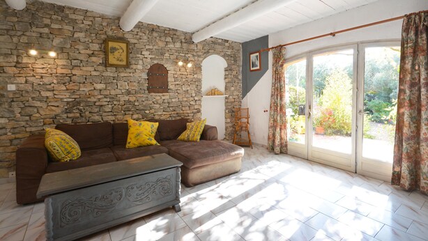 Una sala de estar con pared de piedra, un sofá marrón con cojines amarillos, un mueble de almacenamiento gris y un ventanal con cortinas.