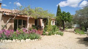 Una casa con techo de tejas, un jardín con senderos de grava y plantas en flor.