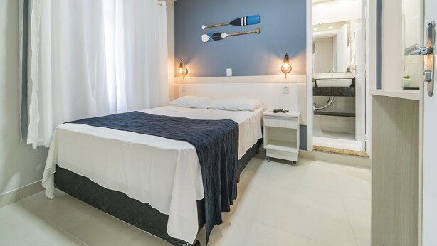 Une chambre à coucher avec un lit, une table de chevet, un miroir et une salle de bain visible à travers une porte ouverte.