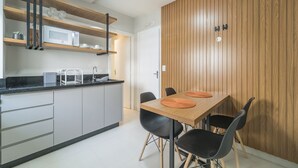 Une cuisine moderne avec un panneau mural en bois, un four à micro-ondes encastré et un coin repas avec des chaises noires et une table en bois.