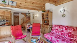 Ein gemütliches Wohnzimmer mit einem roten Sofa, passenden Sesseln und einem Couchtisch mit Snacks und Getränken. Eine Treppe führt zu einem Essbereich mit Holzsesseln und einem Tisch.