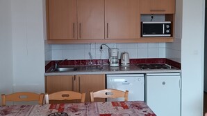 Een compacte keuken met houten kastjes, een magnetron, een koffiezetapparaat en een vaatwasser.