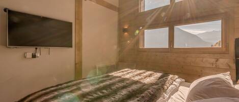 A bedroom with a bed, a TV, and a window with a mountain view.