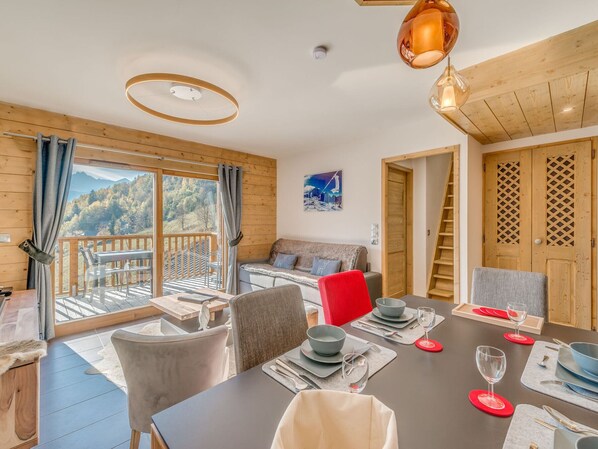 Une pièce moderne avec une table à manger dressée pour quatre personnes, un canapé et une vue sur les montagnes grâce à de grandes fenêtres.