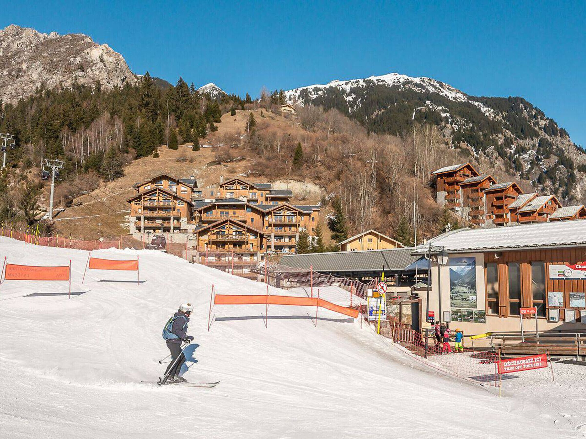 Ein Skigebiet mit Holzhütten, einer Skipiste und einem Berg im Hintergrund.