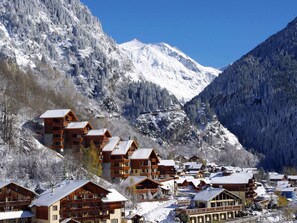 A mountain lodge with multiple wooden buildings, a ski lift, and snow-covered mountains in the background.