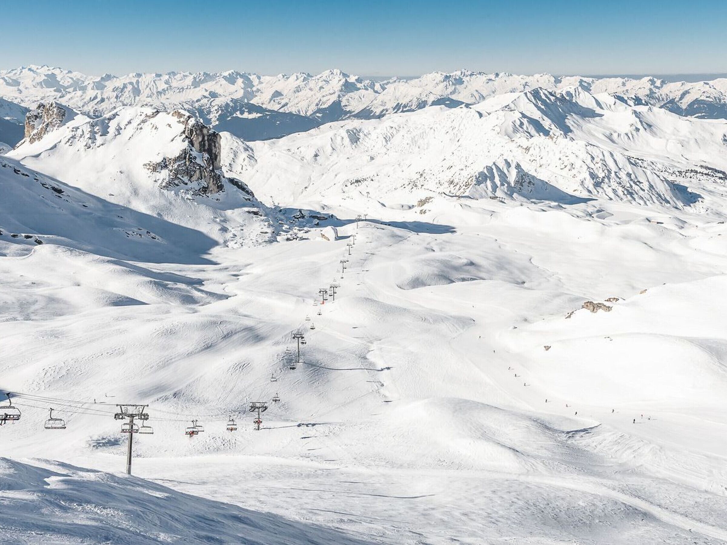 Berglandschap bedekt met sneeuw, met skiliften en een heldere lucht.