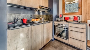 A modern kitchen with wooden cabinets, a stainless steel range hood, a built-in oven, and a window with a view of a forest. - Champagny en Vanoise - Renovated 2-room, 6 pers, balcony, WIFI (Champagny-en-Vanoise)
