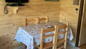 A wooden cabin with a television mounted on the wall, a table with a tablecloth, and a door with a small picture frame.