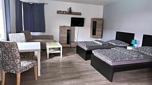 A modern hotel room with a sofa, two beds, a TV, and a desk. - Aparthotel DKS (Chomutov)