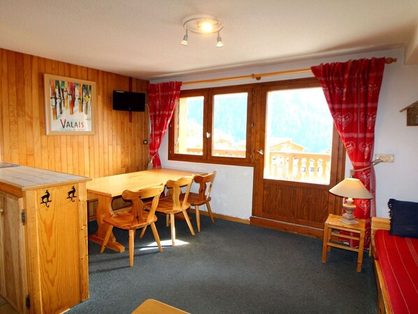 A cozy room with a wooden dining table and chairs, a small sofa, and a window with red curtains. - 3-Room Apartment for 6 People - Pets Allowed - Champagny-en-Vanoise (Champagny-en-Vanoise)