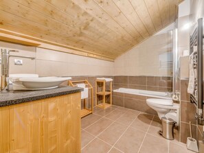 A modern bathroom with a wooden ceiling, a large sink, a bathtub, and a shower area.