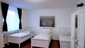 A bedroom with two single beds, a radiator, a window with black curtains, and a framed picture on the wall. - Ferienwohnung Maye Oberhausen (Oberhausen)