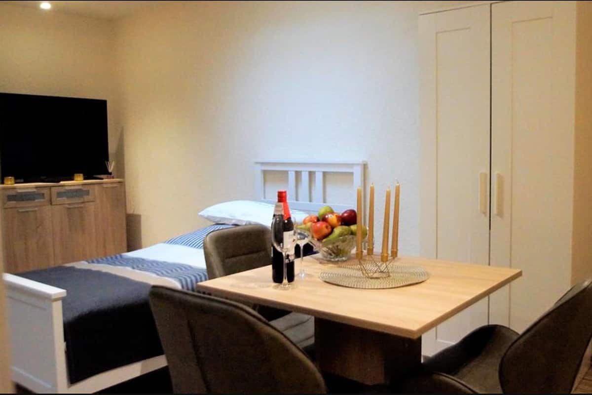 Quarto de hotel com uma cama, uma mesinha com uma fruteira e velas, e uma televisão no canto.