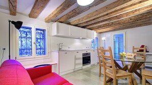 A compact kitchen with white cabinets, a glass dining table, and wooden chairs. - GrandCanal-Red (Venice)