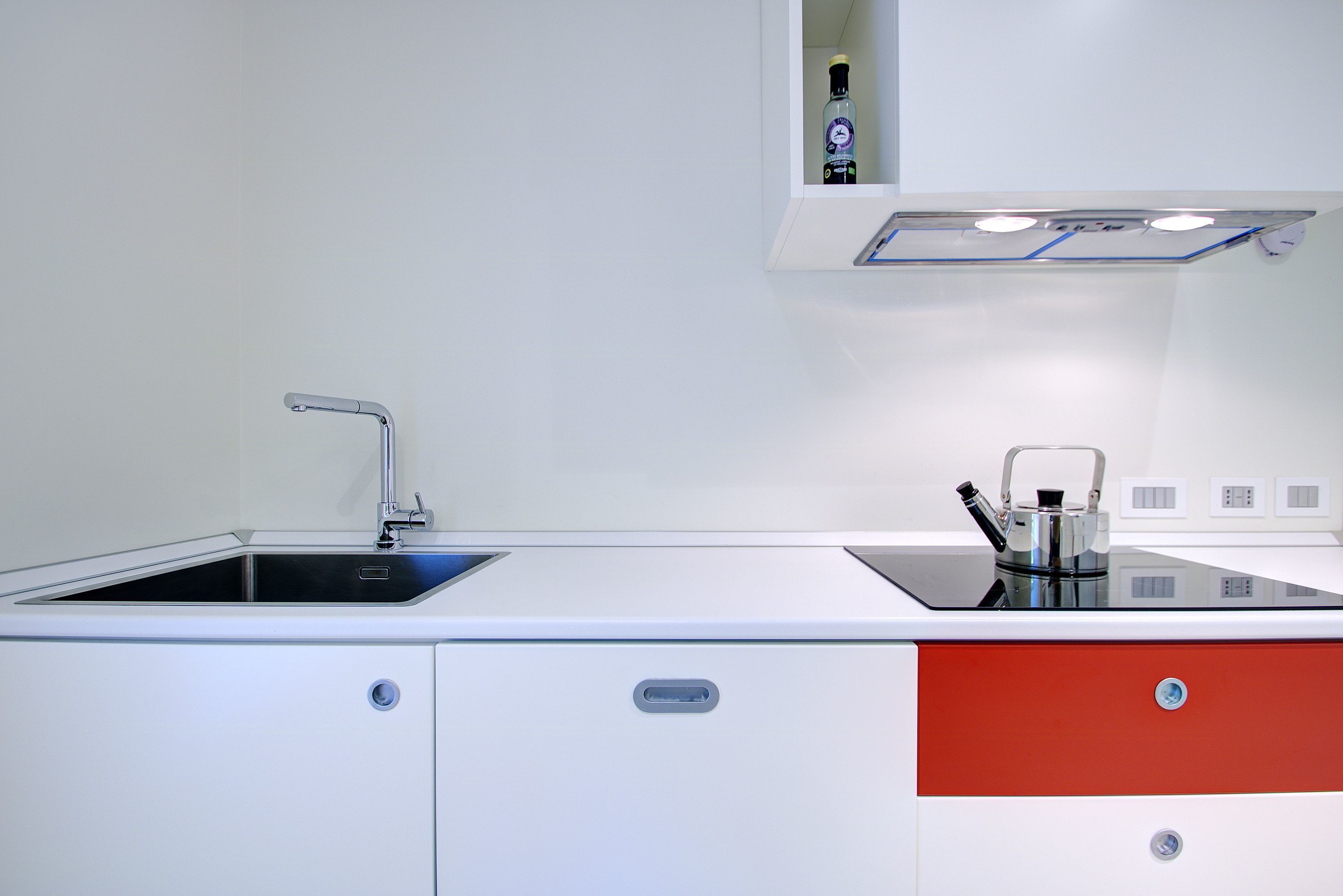 A modern kitchen with a built-in sink, a kettle, and a cabinet with a red drawer.