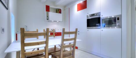 A modern kitchen with white cabinetry, a wooden dining table, and two chairs.