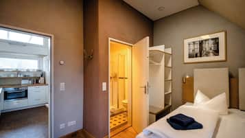 A modern hotel room with a kitchenette, a shower, and a bed with white linens.