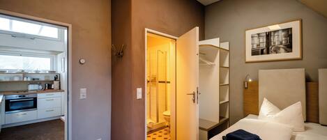 Habitación de hotel moderna con kitchenette, ducha y cama con ropa de cama blanca.