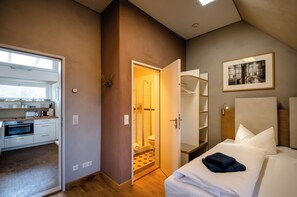 A modern hotel room with a kitchenette, a shower, and a bed with white linens. - Ferienwohnungen Notenbank (Weimar)