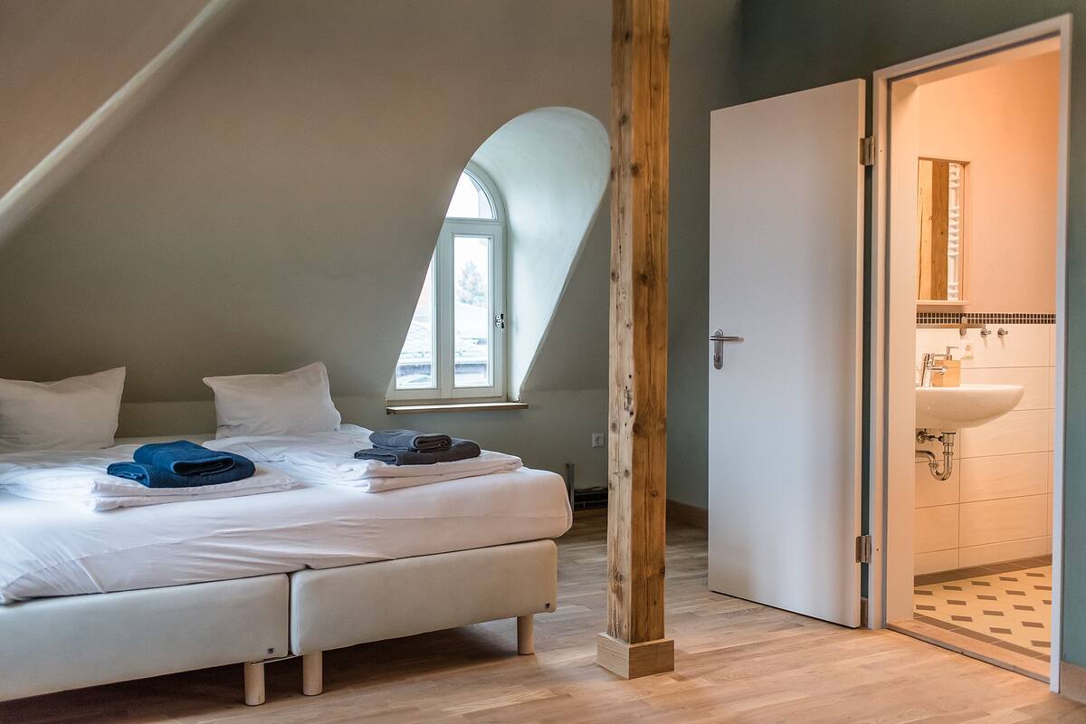 A bedroom with a bed, pillows, a window, and a wooden beam.