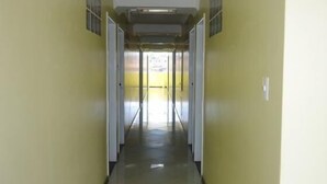 Un pasillo largo y estrecho con paredes amarillas y suelo de baldosas, que lleva a una zona luminosa al final.