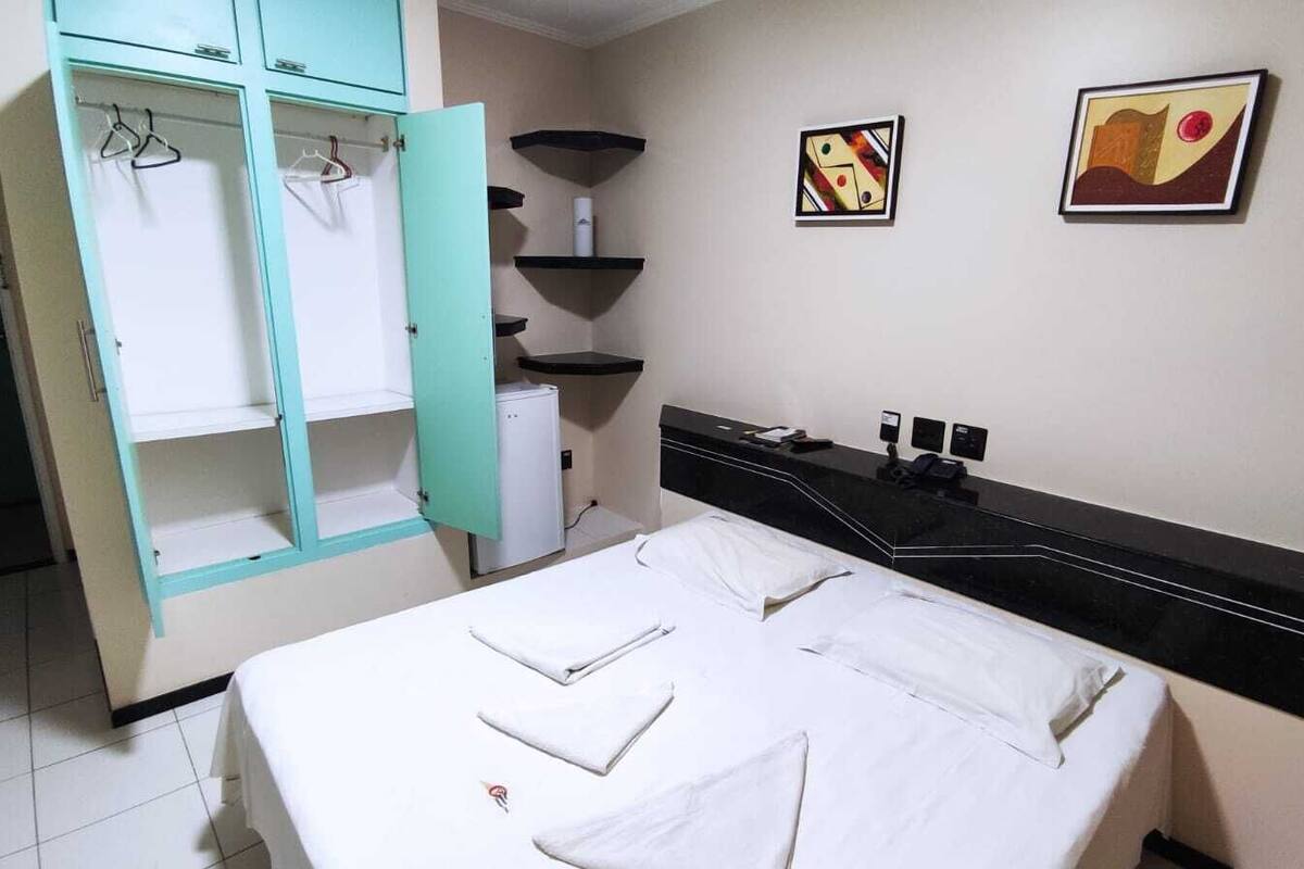 A hotel room with a bed, a wardrobe, a small desk, and two wall-mounted artworks.