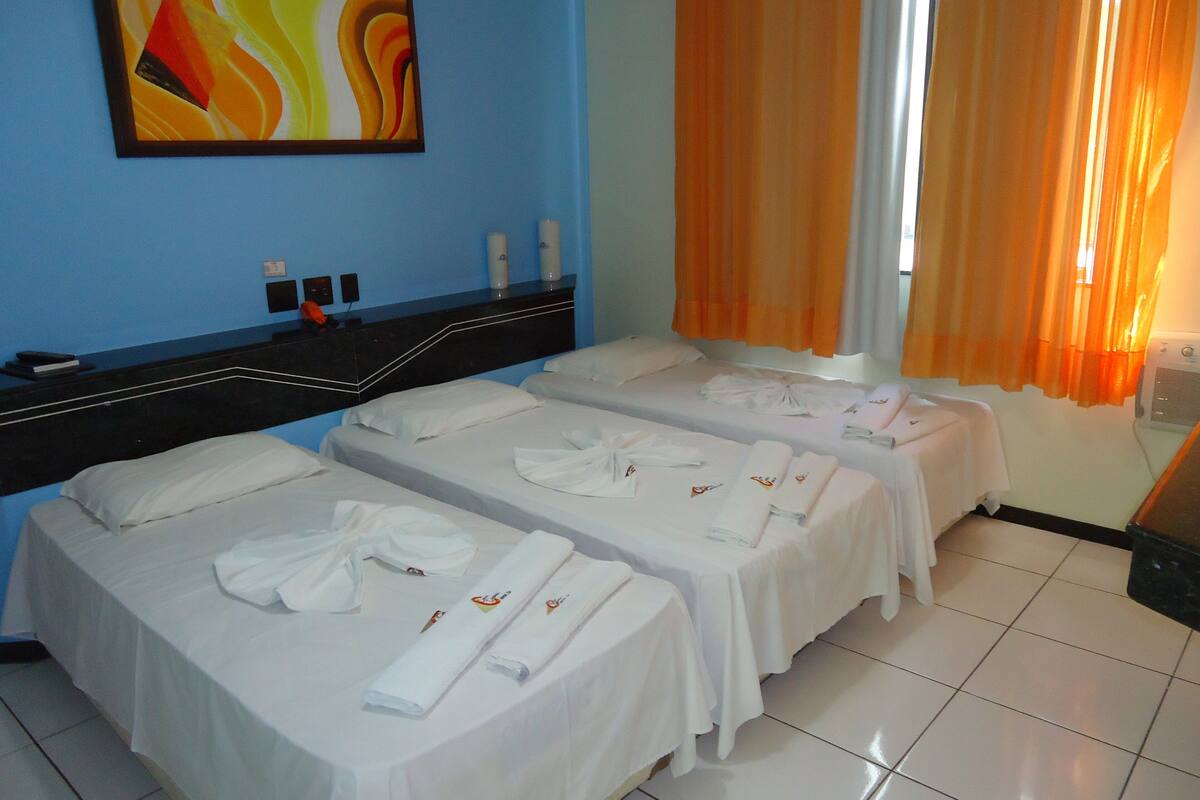 A hotel room with two beds, a desk, a painting on the wall, and orange curtains.