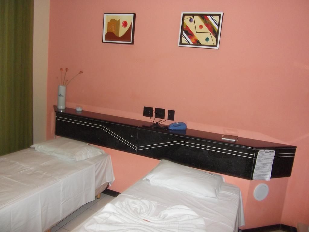 A hotel room with two beds, a black minibar, and two framed artworks on the wall.