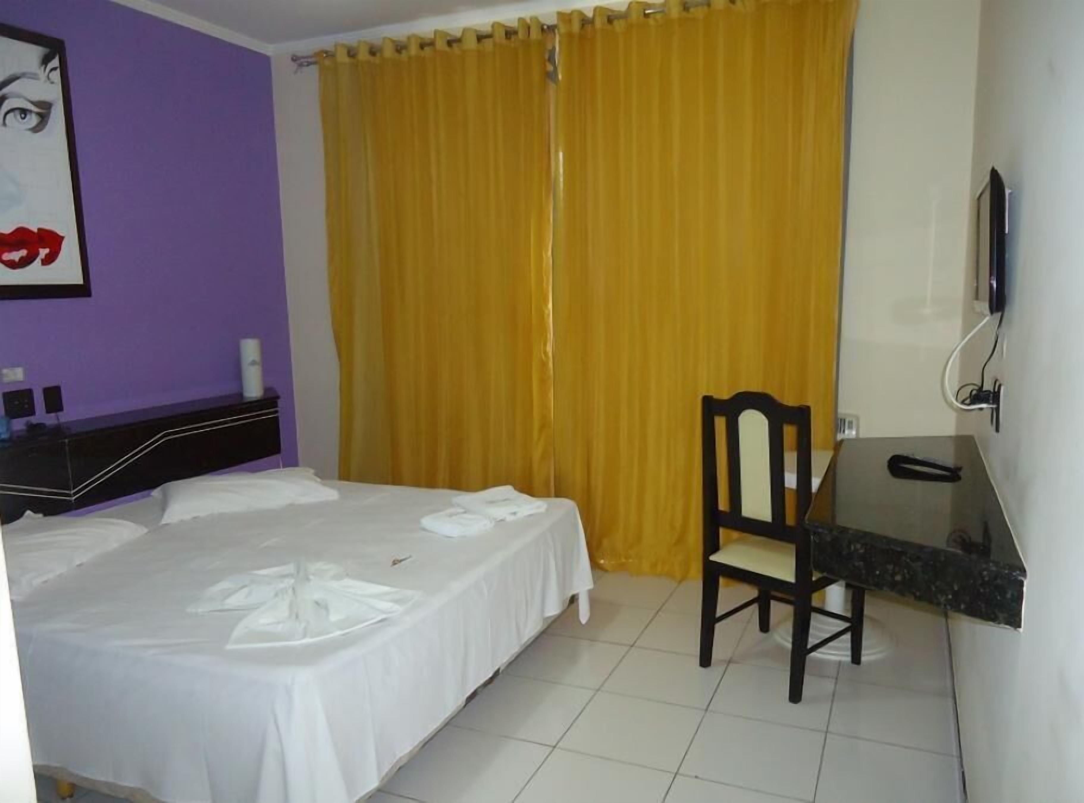 Habitació d'hotel amb un llit, una taula de treball, una cadira i una televisió.