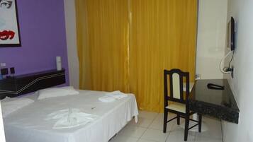 Habitació d'hotel amb un llit, una taula de treball, una cadira i una televisió.