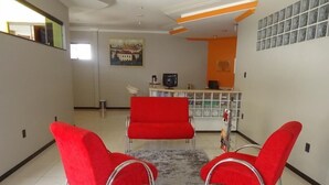Un área de recepción con tres sillas rojas, una alfombra gris, un cuadro en la pared y una barra con un televisor.