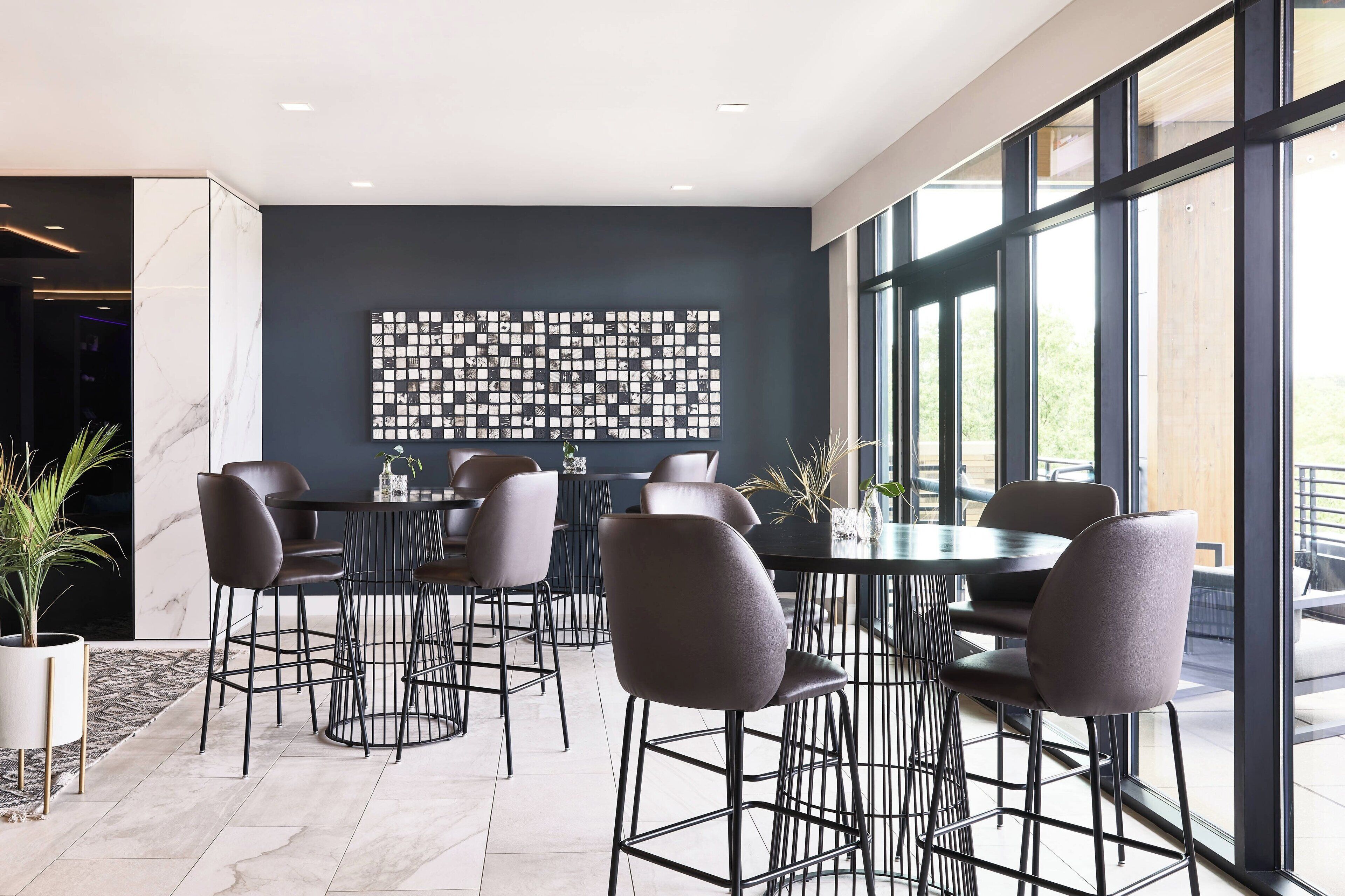 A modern dining area with a black wall art, large windows, and contemporary furniture.