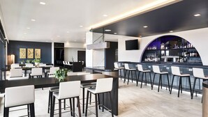 Een moderne bar met een lange toonbank, meerdere krukken en diverse flessen op planken.