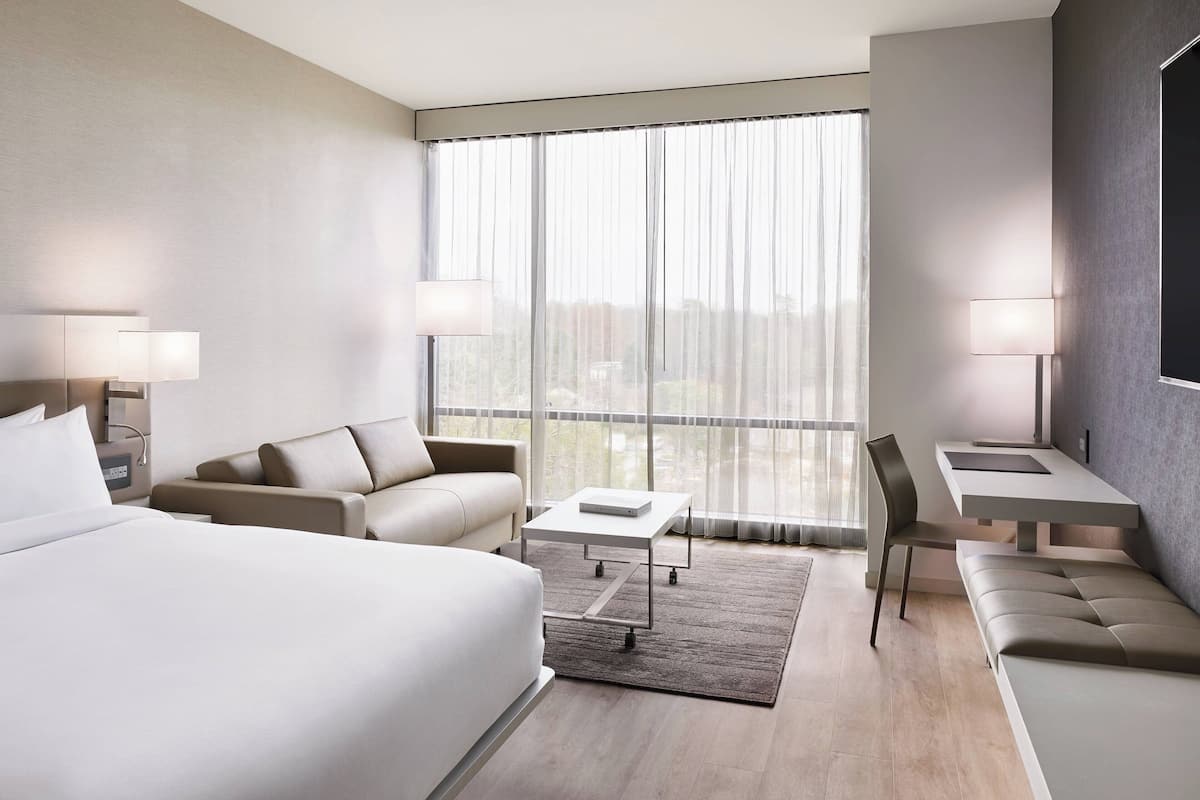 Una habitación de hotel moderna con una cama grande, un sofá, una mesita y un escritorio con una silla.