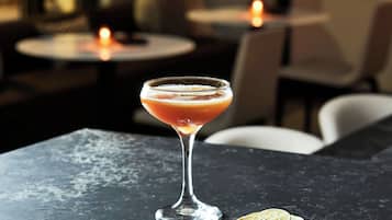 A cocktail in a martini glass on a dark marble table with a slice of lime and a lemon wedge beside it.