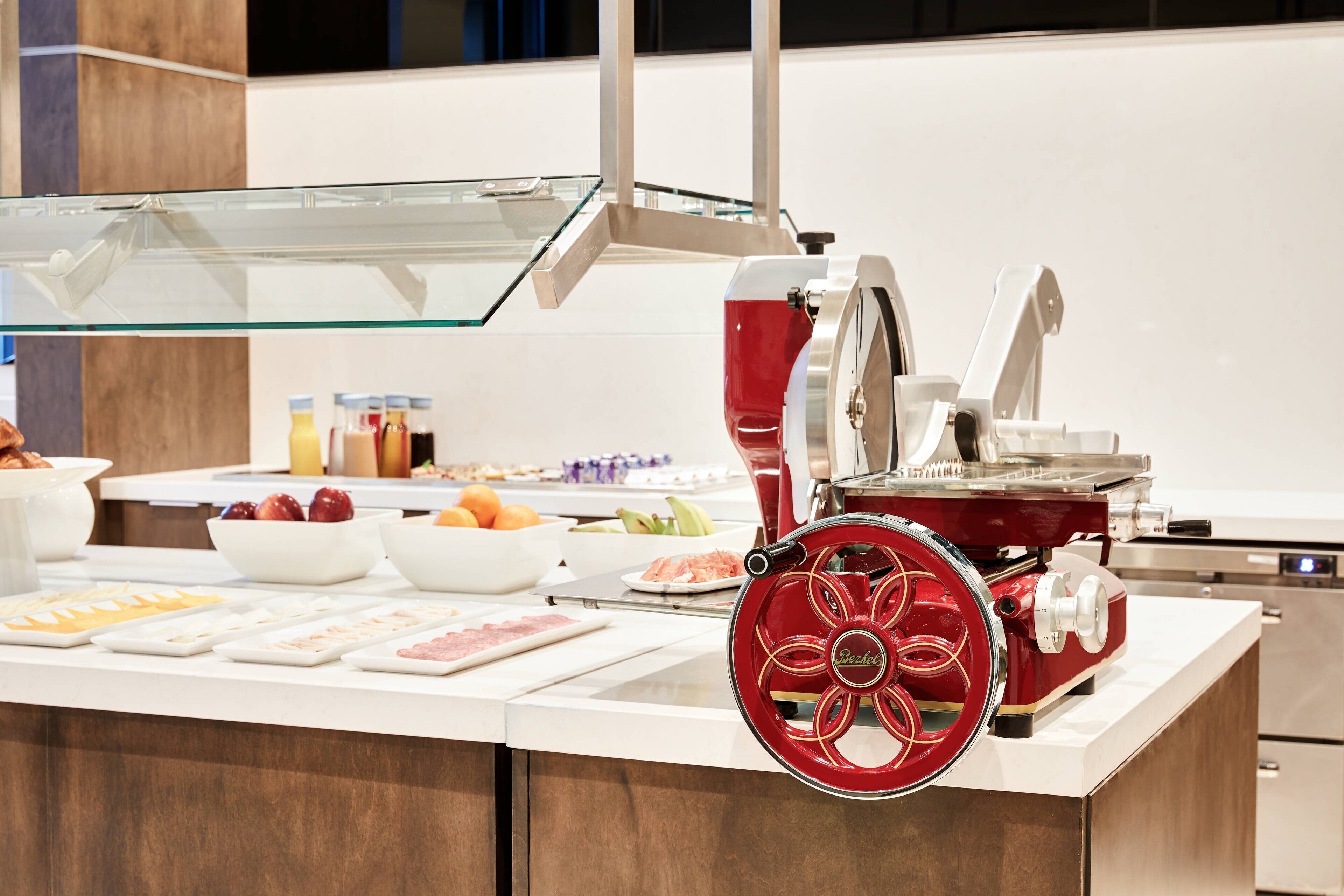 A buffet setup with a red food processor, various bowls of fruits and vegetables, and a glass display case.