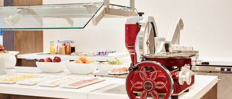 A buffet setup with a red food processor, various bowls of fruits and vegetables, and a glass display case.