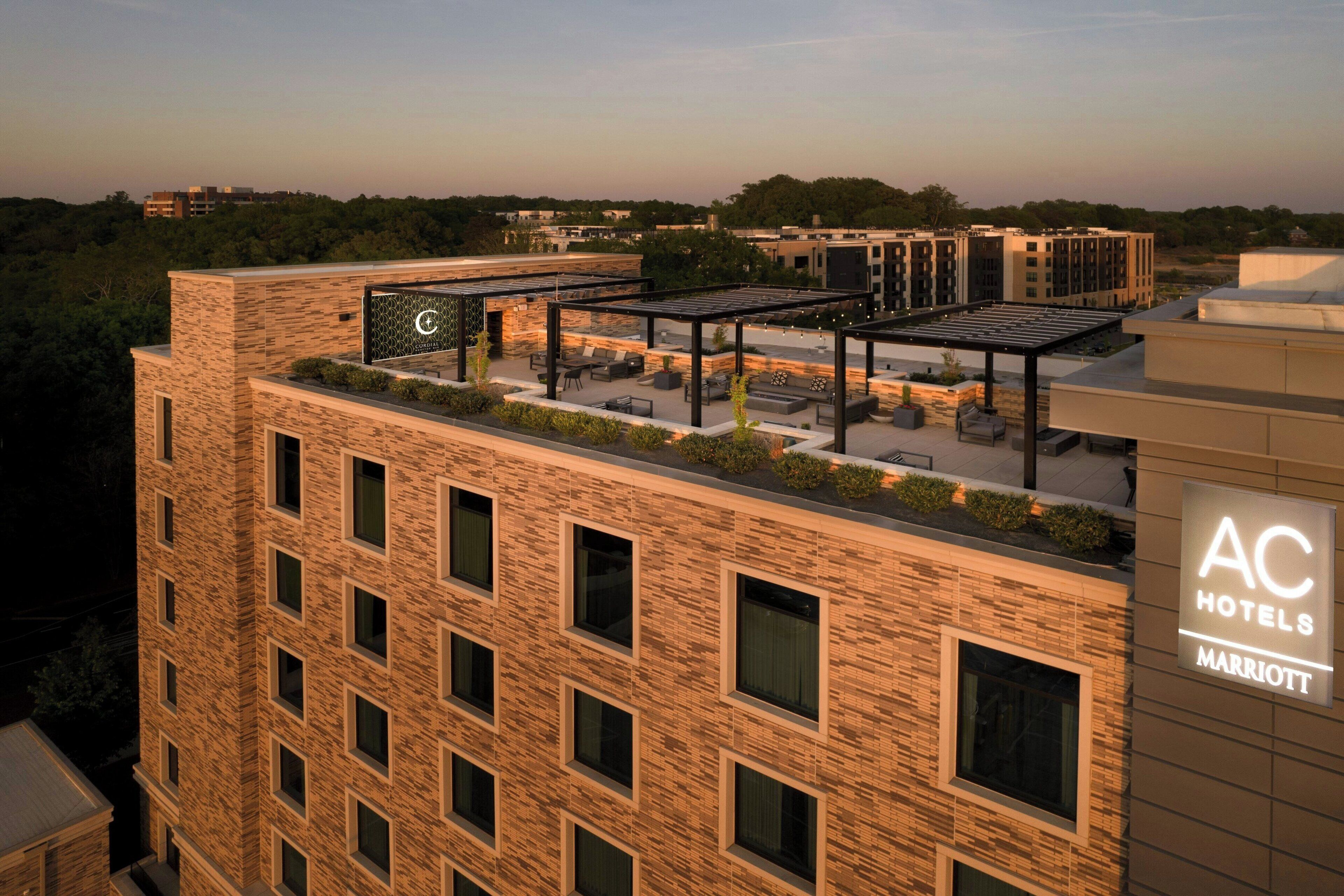 A hotel with a rooftop patio area, multiple windows, and a sign indicating it is part of the AC Hotels Marriott chain.