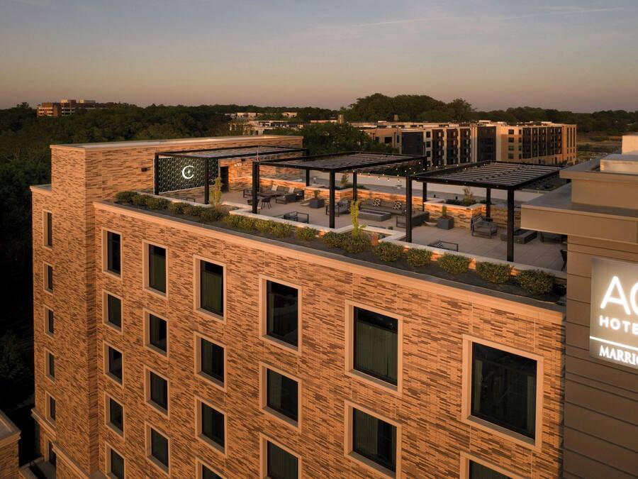 A hotel with a rooftop patio area, multiple windows, and a sign indicating it is part of the AC Hotels Marriott chain.