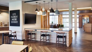 Eine moderne Bar mit einer zentralen Barinsel, Barhocker, Pendelleuchten und einem großen Flachbildfernseher an der Wand.