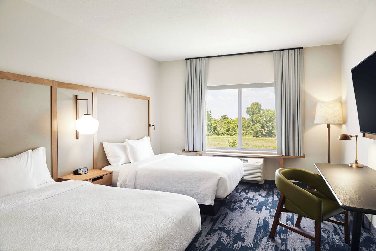 A hotel room with two beds, a desk, a chair, a TV, and a window with curtains.