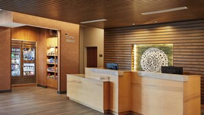 Ein Hotel-Rezeptionsbereich mit einem Holzbüro, einer Eck-Kiosk-Abteilung mit Kühlregalen und einem Wanddekor.