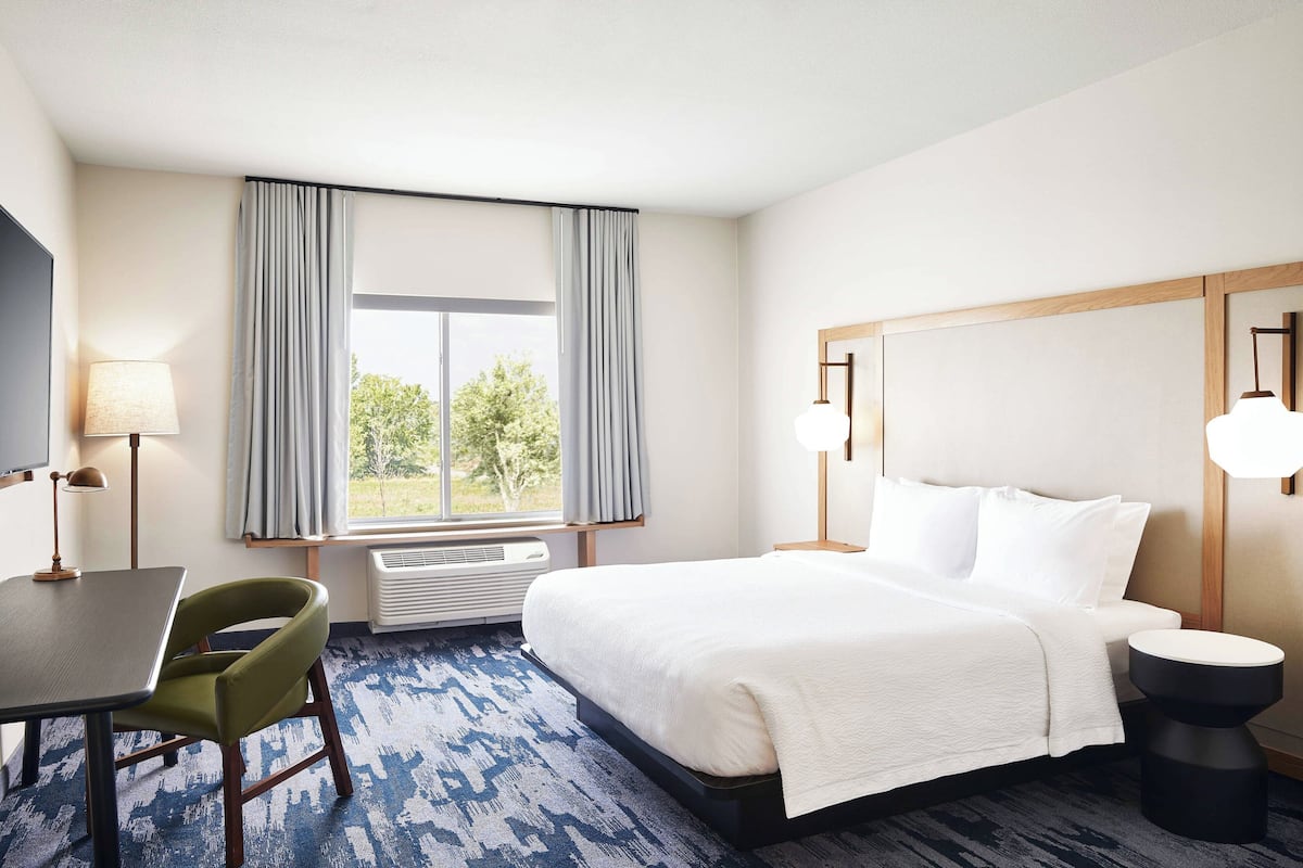 A hotel room with a bed, a desk, a chair, a lamp, and a window with curtains.