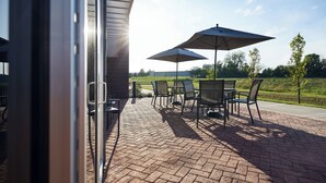 Eine Terrasse im Freien mit Backsteinböden, Metallstühlen und zwei großen Sonnenschirmen.