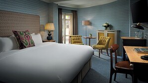 Quarto de hotel com uma cama grande, duas poltronas, uma mesinha, uma escrivaninha e uma televisão.