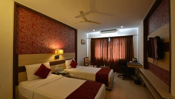 A hotel room with two beds, a desk, a chair, a TV, and a ceiling fan.