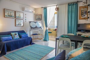 A living room with a blue sofa, a dining table with chairs, a TV, and nautical-themed decorations. - Casa nel blu (Polignano a Mare)