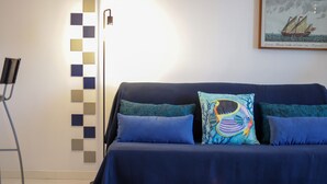 Una habitación con un sofá azul oscuro, dos almohadas a juego, un cuadro en la pared y una silla.