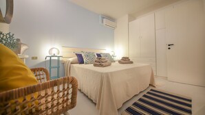Un dormitorio con cama, mesitas de noche, una silla, armario y una alfombra a rayas.